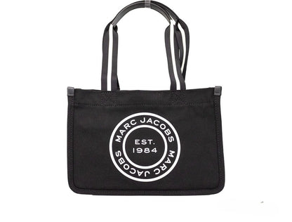 Medium Travel Tote Shoulder Bag by Marc Jacobs for women in canvas black & silver presents a statuesque silhouette, showcasing a secure zipper and statuesque with versatile handle for a sophisticated look.