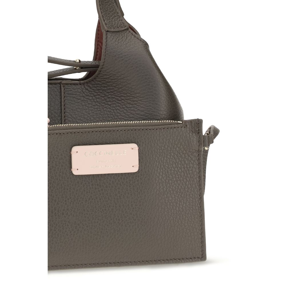 Small Crossbody Oval Handbag by Coccinelle for women in bos taurus calf grained leather brown & gold features an refined silhouette, showcasing a secure zipper & button, ample , and versatile crossbody-strap, shoulder-strap, handle, adjustable-strap & detachable-strap for a sophisticated refined aesthetic.