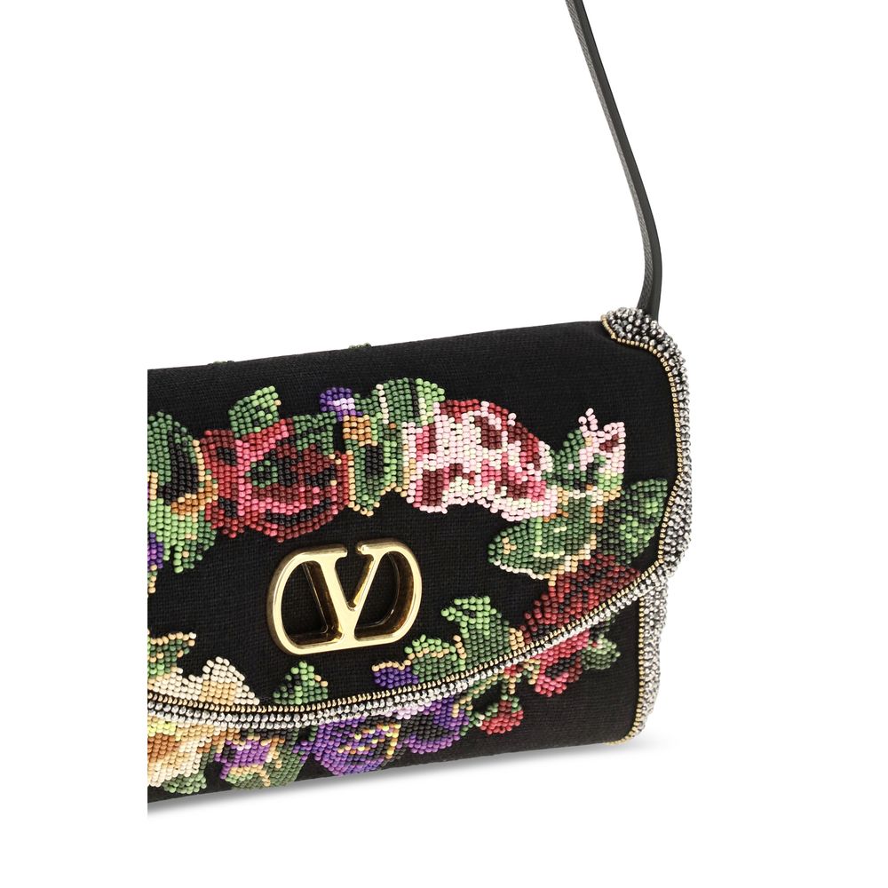 Small Shoulder Bag by Valentino Garavani for women in calfskin leather & linen black, gold, floral & signature features an effortlessly chic silhouette with a secure magnetic & buckle, ample single-compartment, and versatile shoulder-strap, adjustable-strap & handle for effortlessly chic everyday luxury.